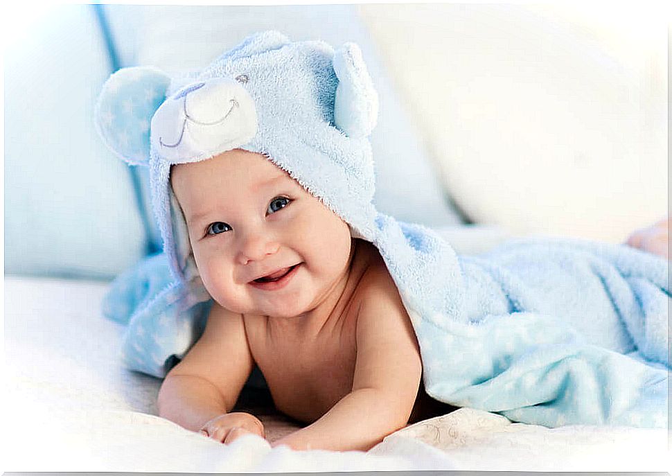 Baby lying on his stomach wrapped in a blue towel with a bear-shaped hat.